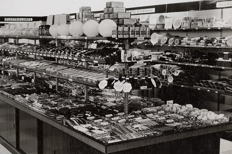 One of Woolworths' first self-service island counters.  Extension pieces have been used to display extra tiers of shelving above the main tabletop and lockable understocks cupboards (holding reserve stock to fill up with) were incorporated in the early designs.