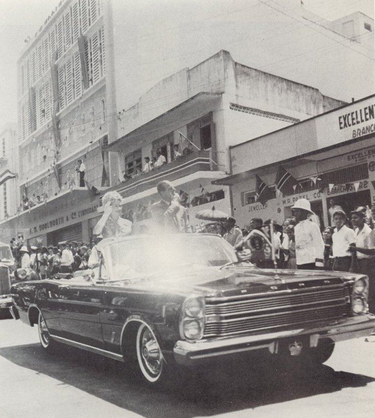 Her Majesty Queen Elizabeth II and His Royal Highness Prince Philip drive past Woolworths on a state visit to Trinidad and Tobago in the 1960s